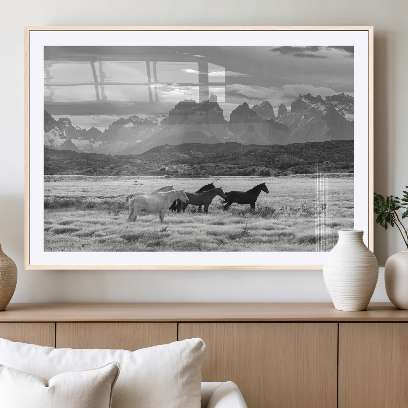 A black and white landscape of wild horses grazing in a vast grassland with towering mountains in the background, creating a moody and rustic western aesthetic.