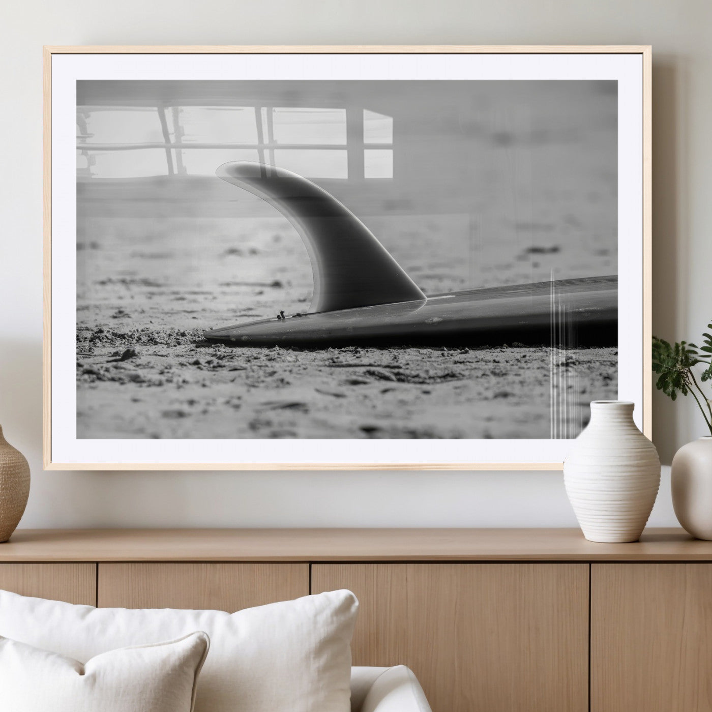 A black and white close-up of a surfboard fin resting on the sandy shore, highlighting minimalist beach aesthetics and classic surf culture.