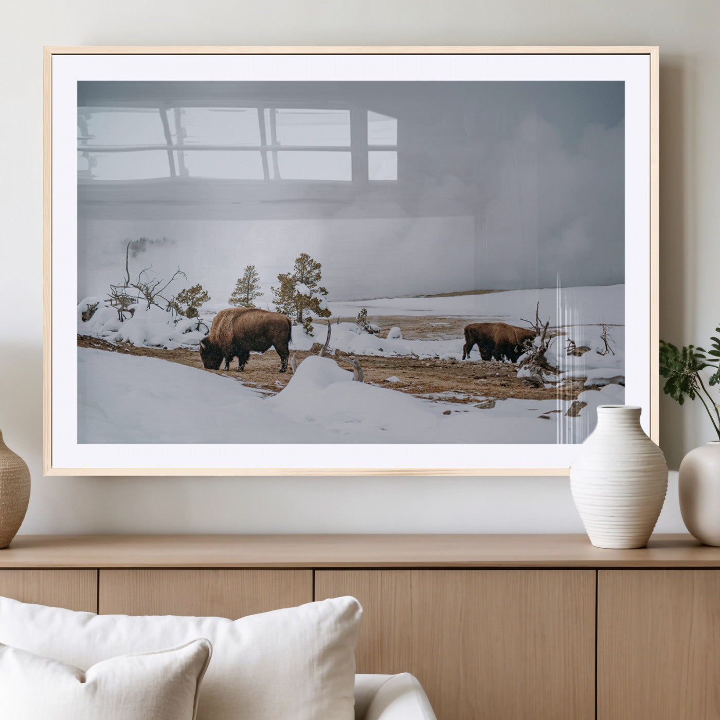 Two bison grazing in a snowy open landscape with misty hills in the background, creating a peaceful and rustic winter scene.