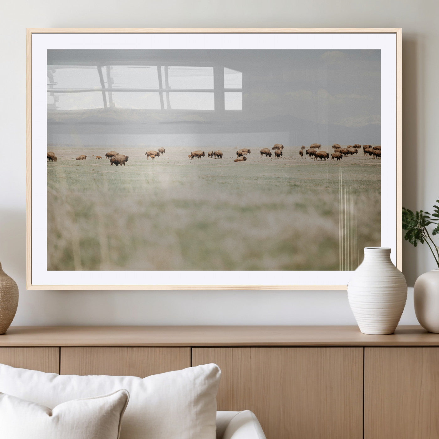 A herd of bison grazing in an open prairie with distant mountains under a soft sky, creating a serene and rustic Western landscape.