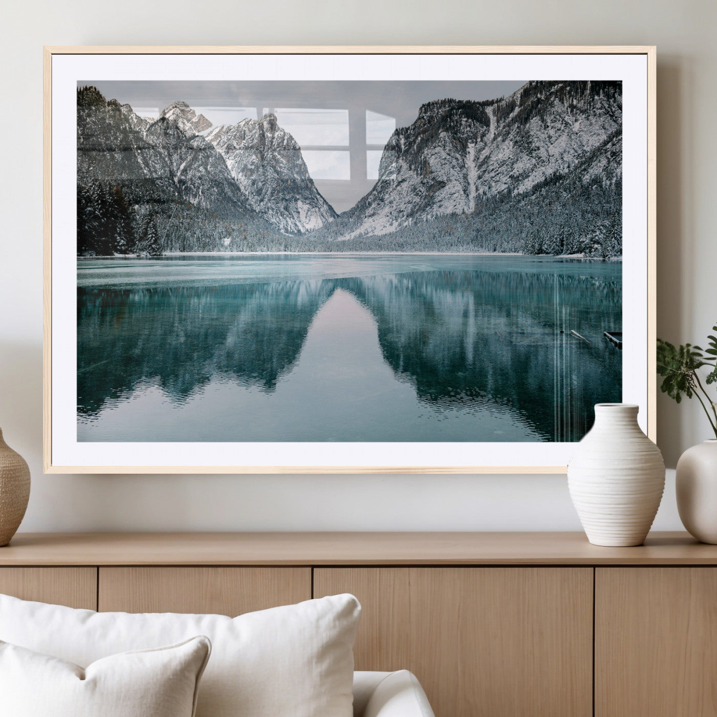 Crystal-clear alpine lake reflecting snow-covered mountains, surrounded by evergreen trees, creating a serene and tranquil winter landscape.