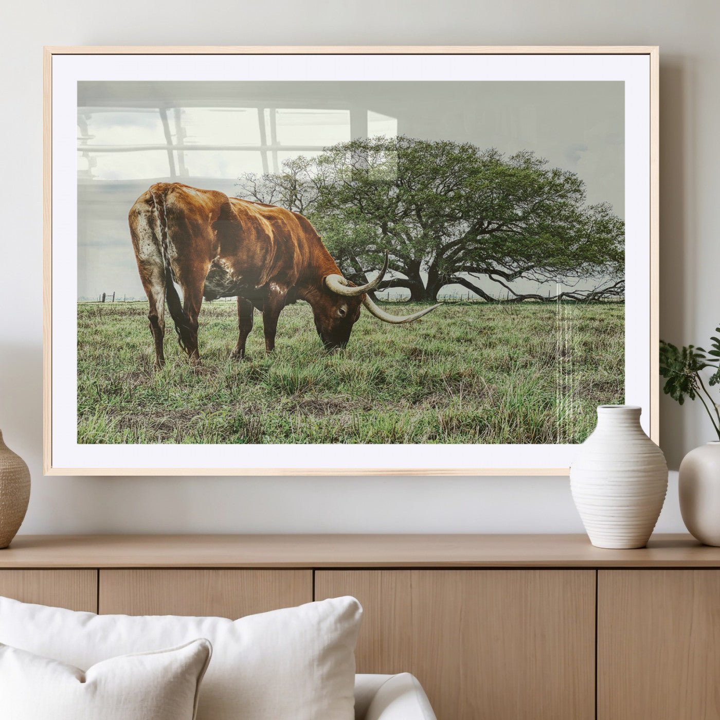 A Texas Longhorn grazing in a green pasture with a large tree in the background, evoking a rustic Western and farmhouse aesthetic.