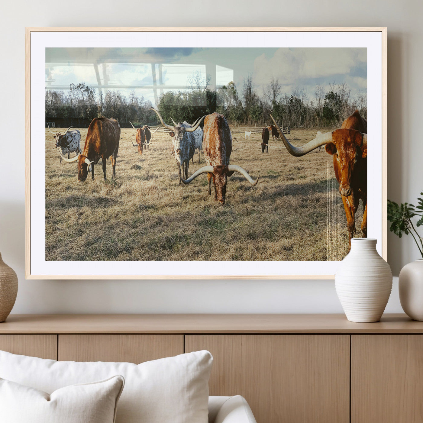 A herd of Texas Longhorn cattle grazing in an open field under a partly cloudy sky, capturing a rustic and Western ranch aesthetic.