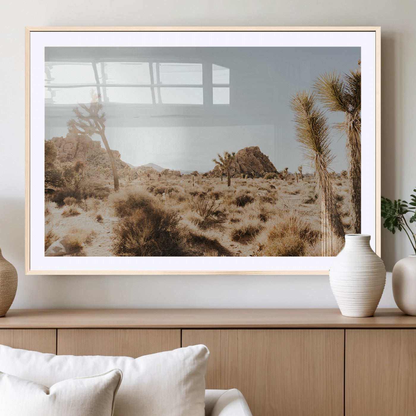 Sunlit desert landscape featuring Joshua trees, rocky formations, and dry bushes under a clear sky.