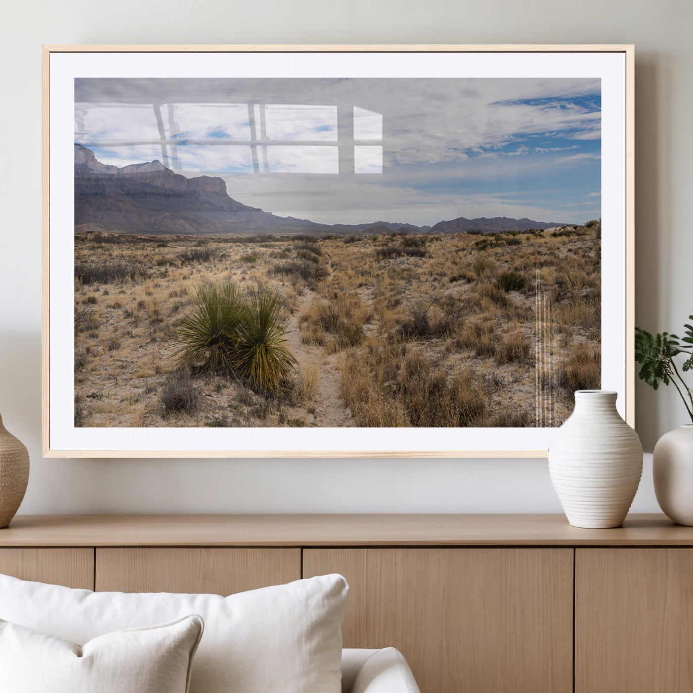 A scenic desert landscape with dry grasses, scattered shrubs, and a distant mountain range under a partly cloudy blue sky.