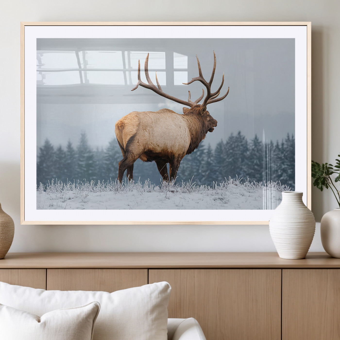 A majestic elk standing in a snowy landscape, with large antlers, set against a backdrop of evergreen trees and a soft winter sky.