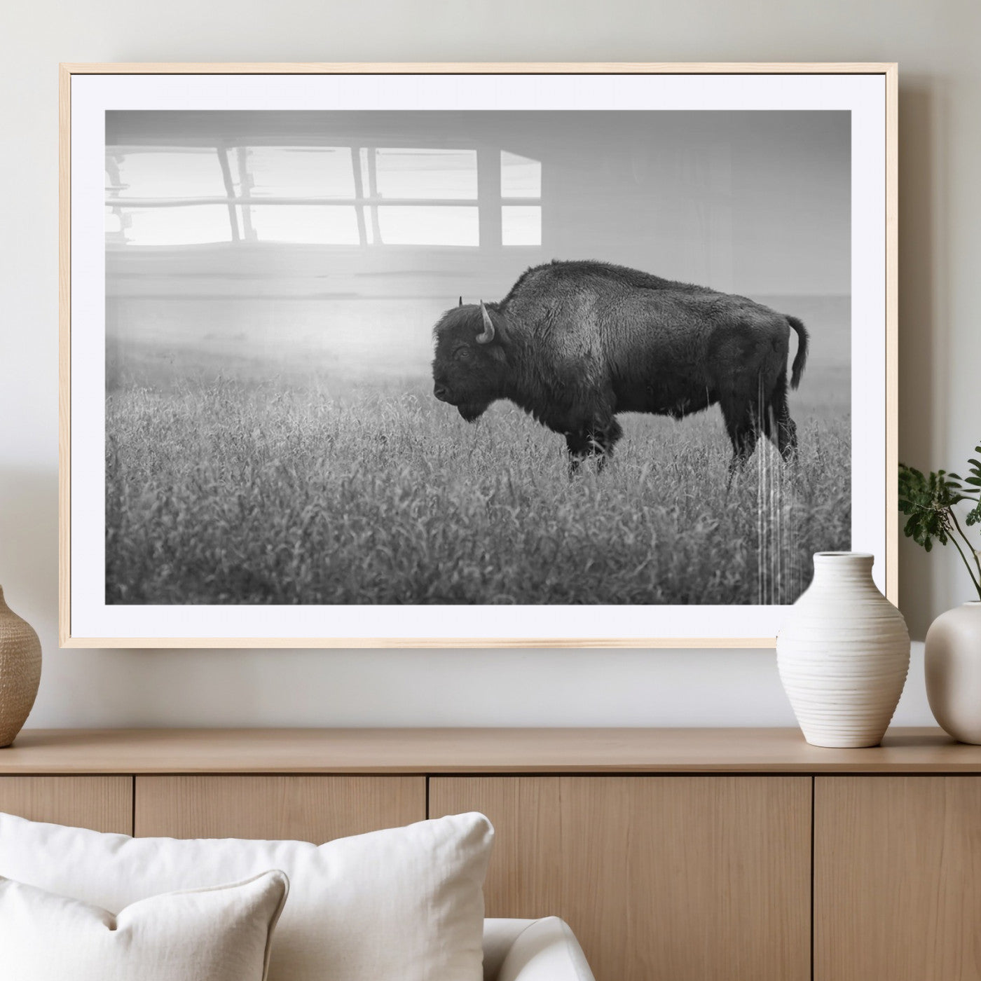 "Black and white image of a bison grazing in a vast field under an overcast sky."