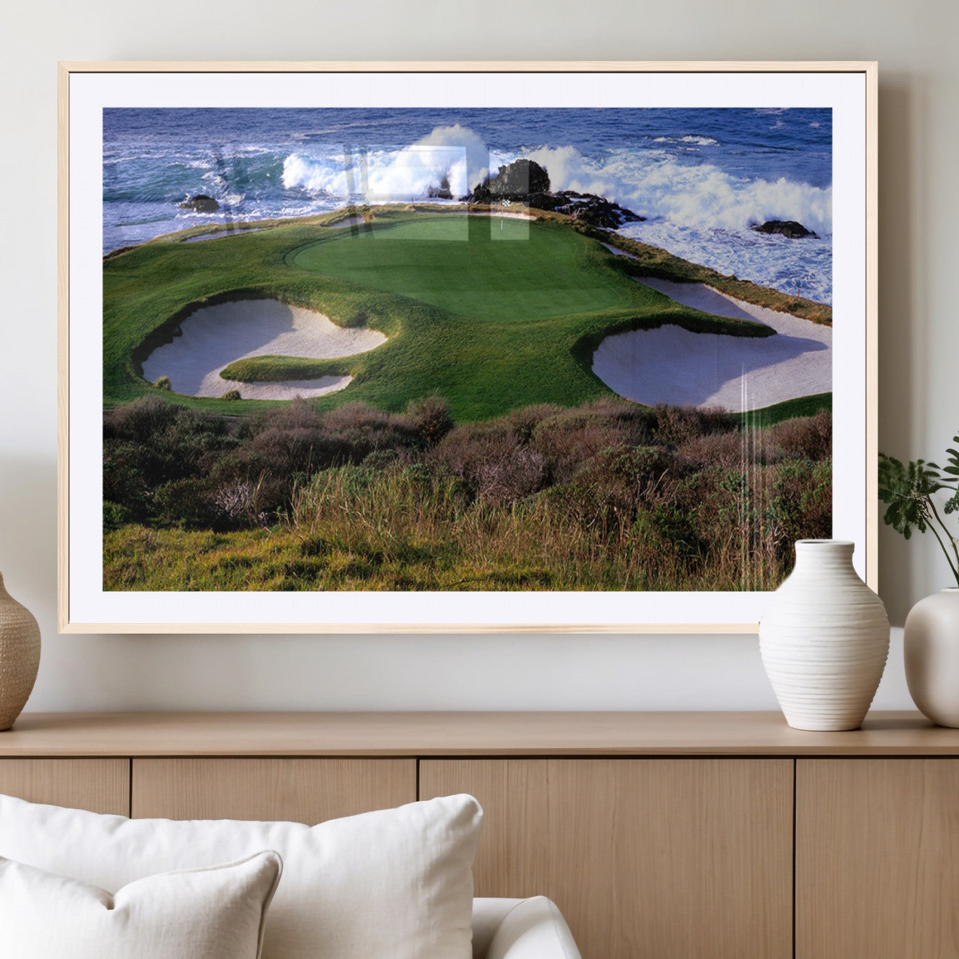 A scenic golf course located by the ocean, featuring a well-manicured green surrounded by sand traps and powerful ocean waves crashing on the shore.
