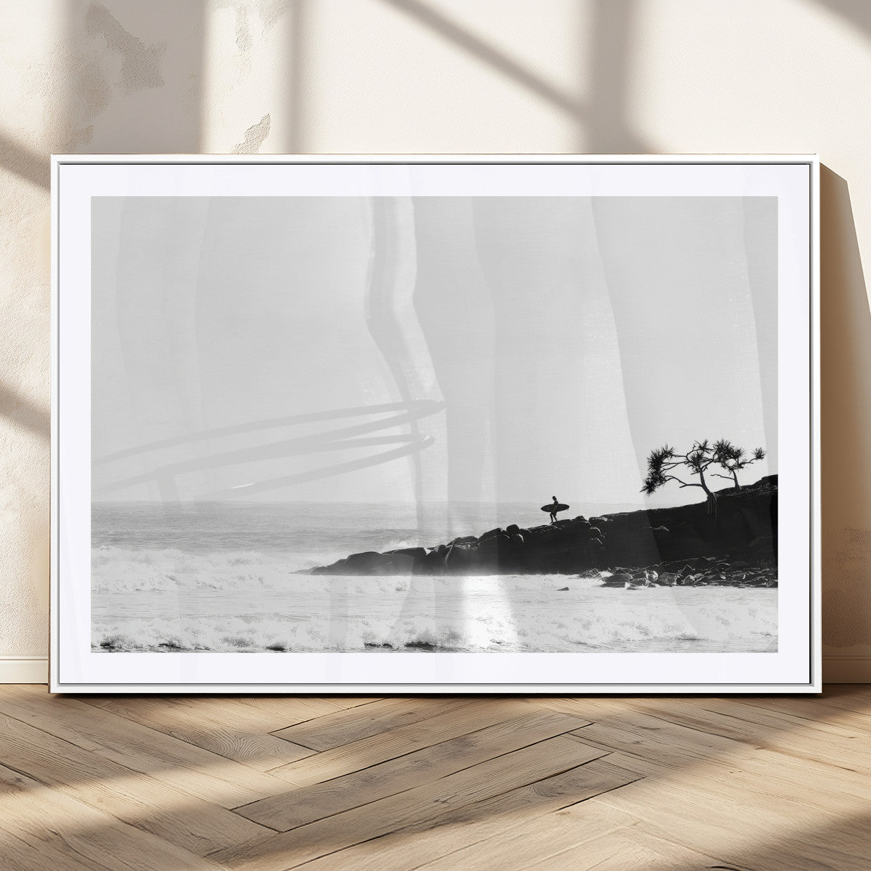 Black and white photo of a surfer standing on rocky cliffs, gazing at the waves, embodying the spirit of adventure and solitude.