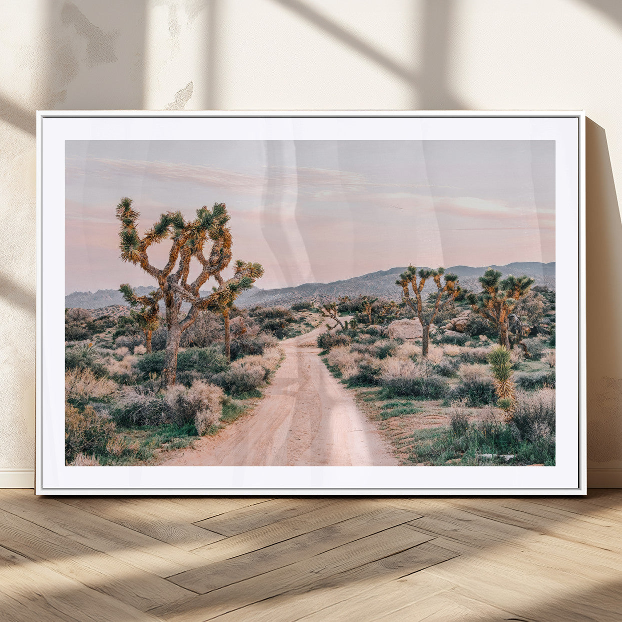 A dusty road winding through Joshua Tree National Park, framed by iconic twisted trees and warm desert tones under a soft pastel sky.