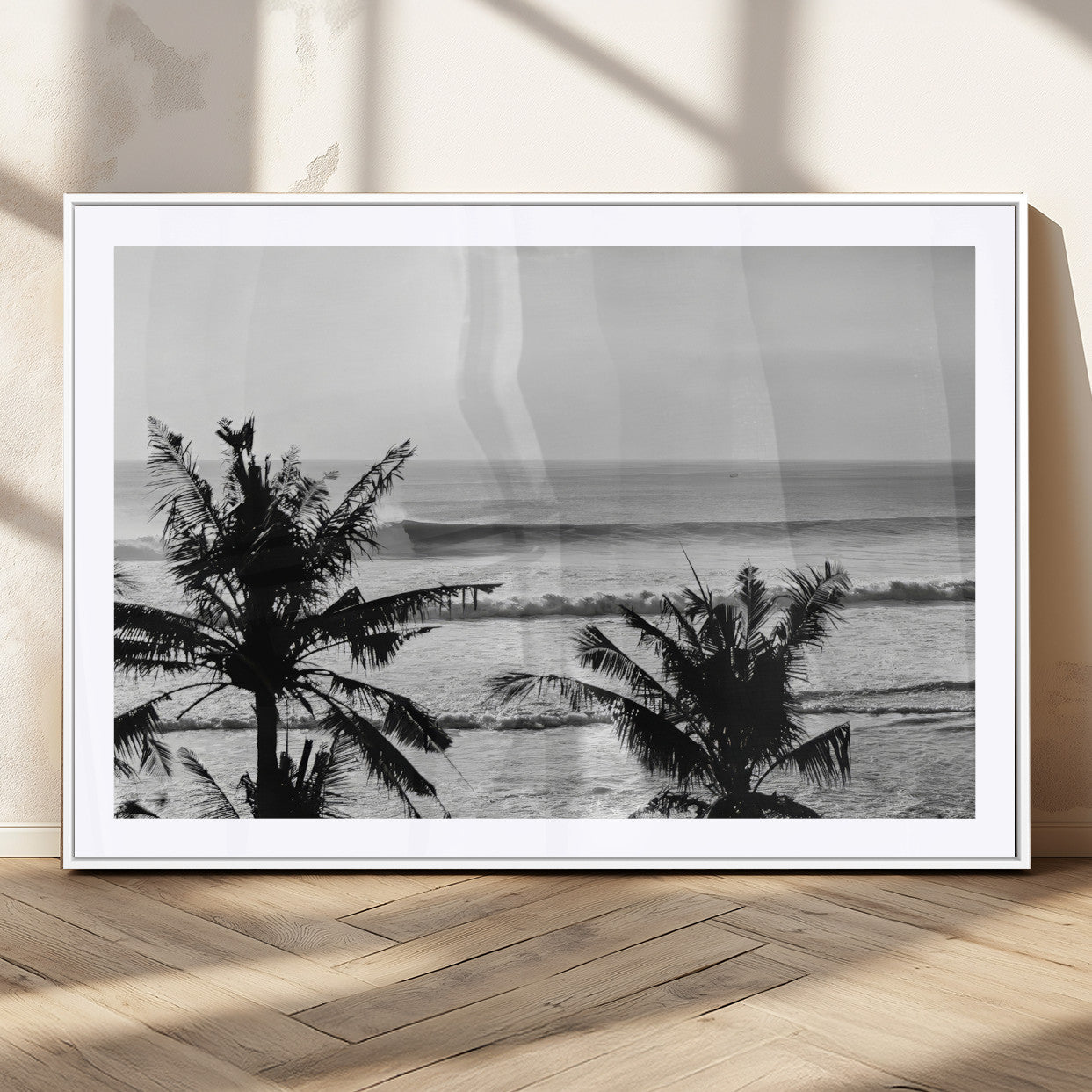 Black and white view of ocean waves crashing on a tropical coastline, framed by silhouetted palm trees under a vast, open sky.