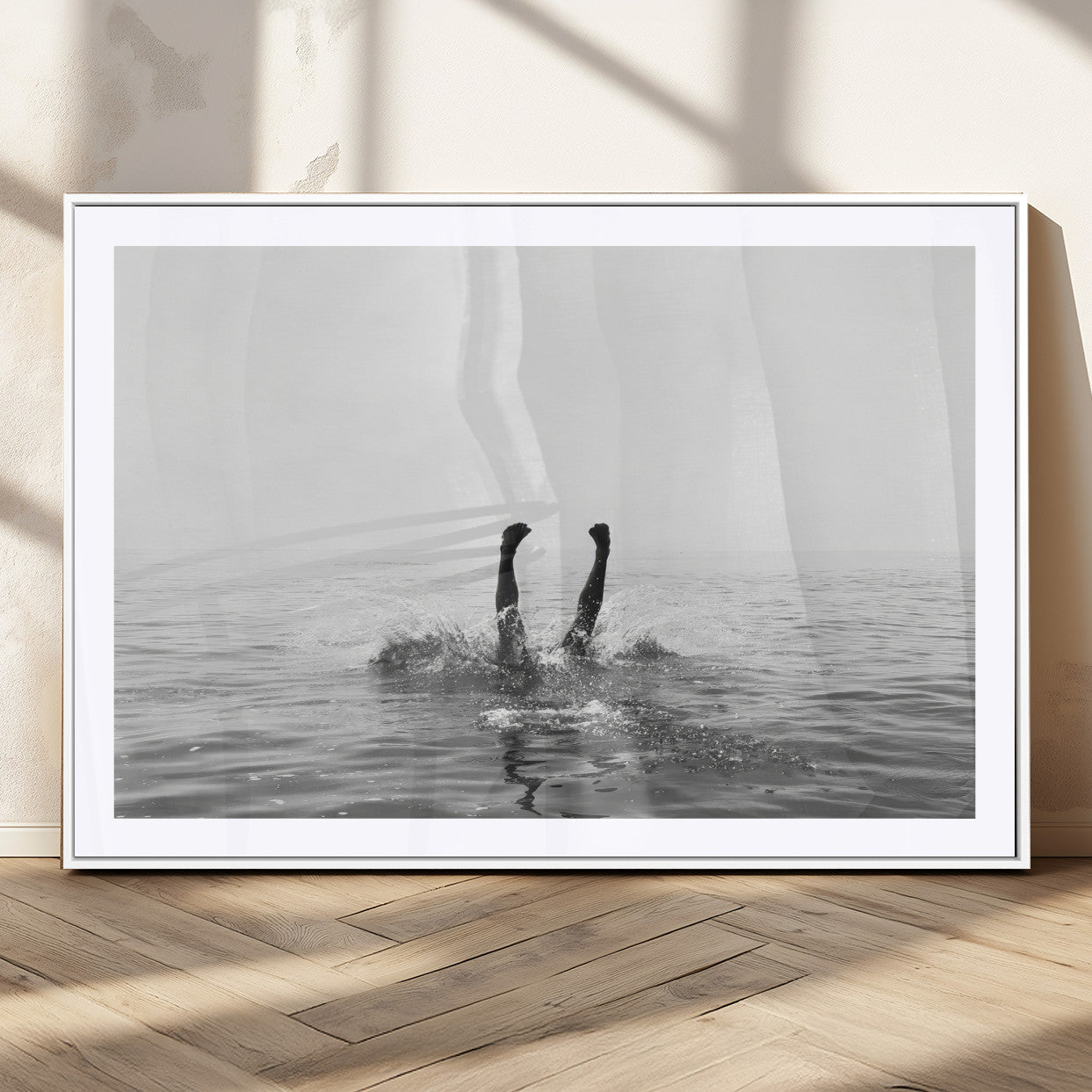 A black and white minimalist water scene capturing a playful splash as a swimmer dives upside down, creating a carefree and artistic aquatic aesthetic.
