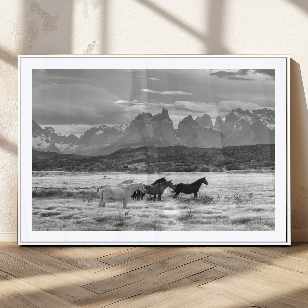 A black and white landscape of wild horses grazing in a vast grassland with towering mountains in the background, creating a moody and rustic western aesthetic.