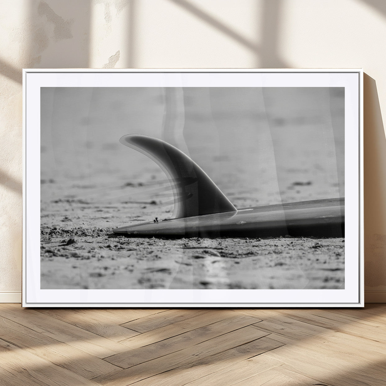 A black and white close-up of a surfboard fin resting on the sandy shore, highlighting minimalist beach aesthetics and classic surf culture.