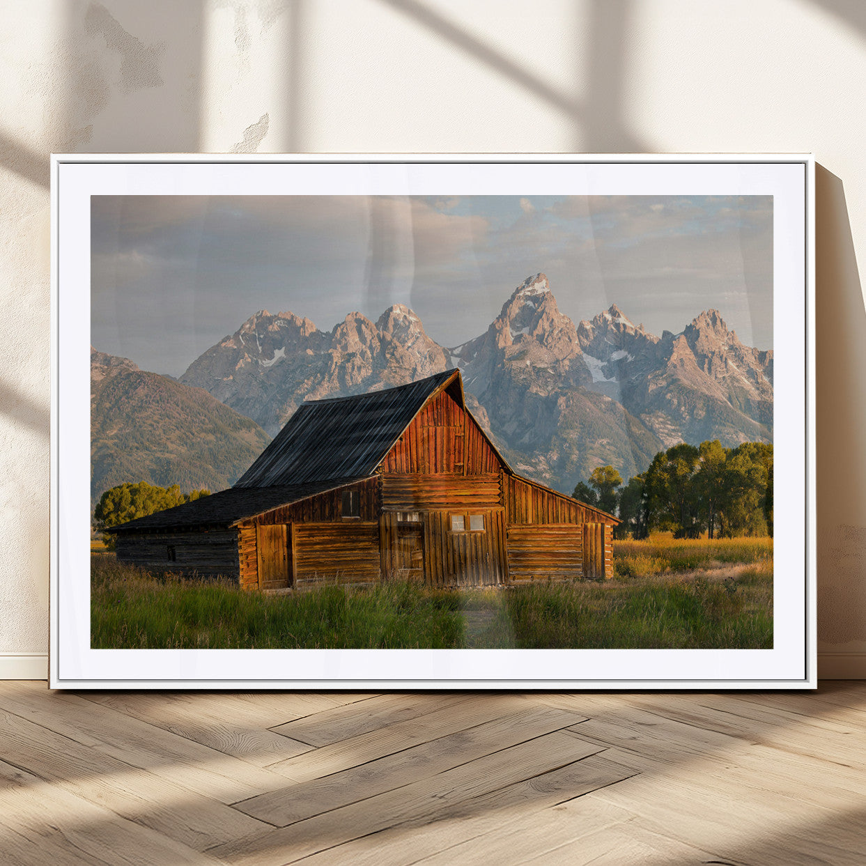 Rustic wooden barn set against towering mountain peaks under warm golden light, creating a peaceful Western countryside scene.