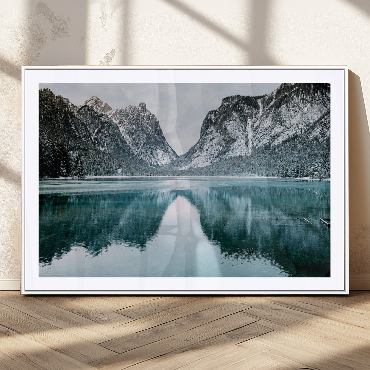 Crystal-clear alpine lake reflecting snow-covered mountains, surrounded by evergreen trees, creating a serene and tranquil winter landscape.