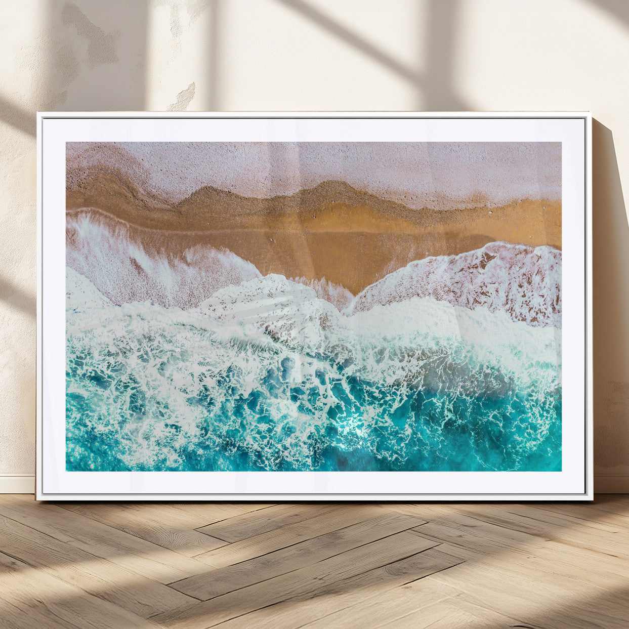 Aerial view of ocean waves crashing onto a sandy beach, with turquoise water and foamy white surf, creating a serene coastal aesthetic for home decor.