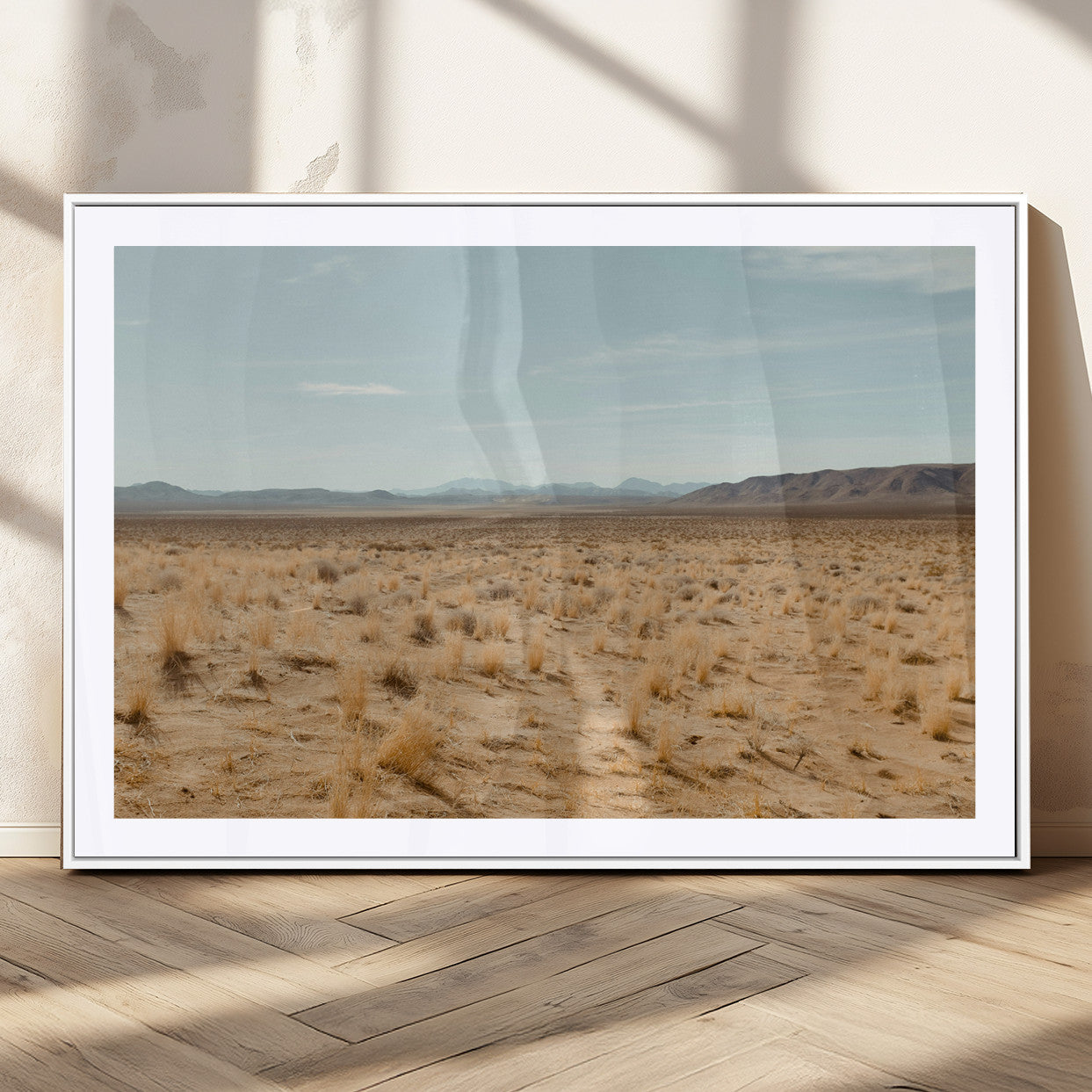 Expansive desert landscape with scattered dry grass and distant mountain range under a pale blue sky – Wall Art Canvas Print.