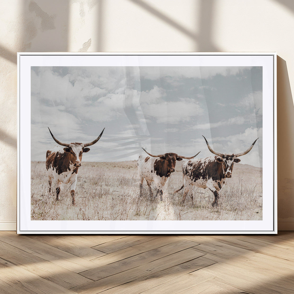 Three Texas Longhorn cattle walking through a dry grassy field under a partly cloudy sky.