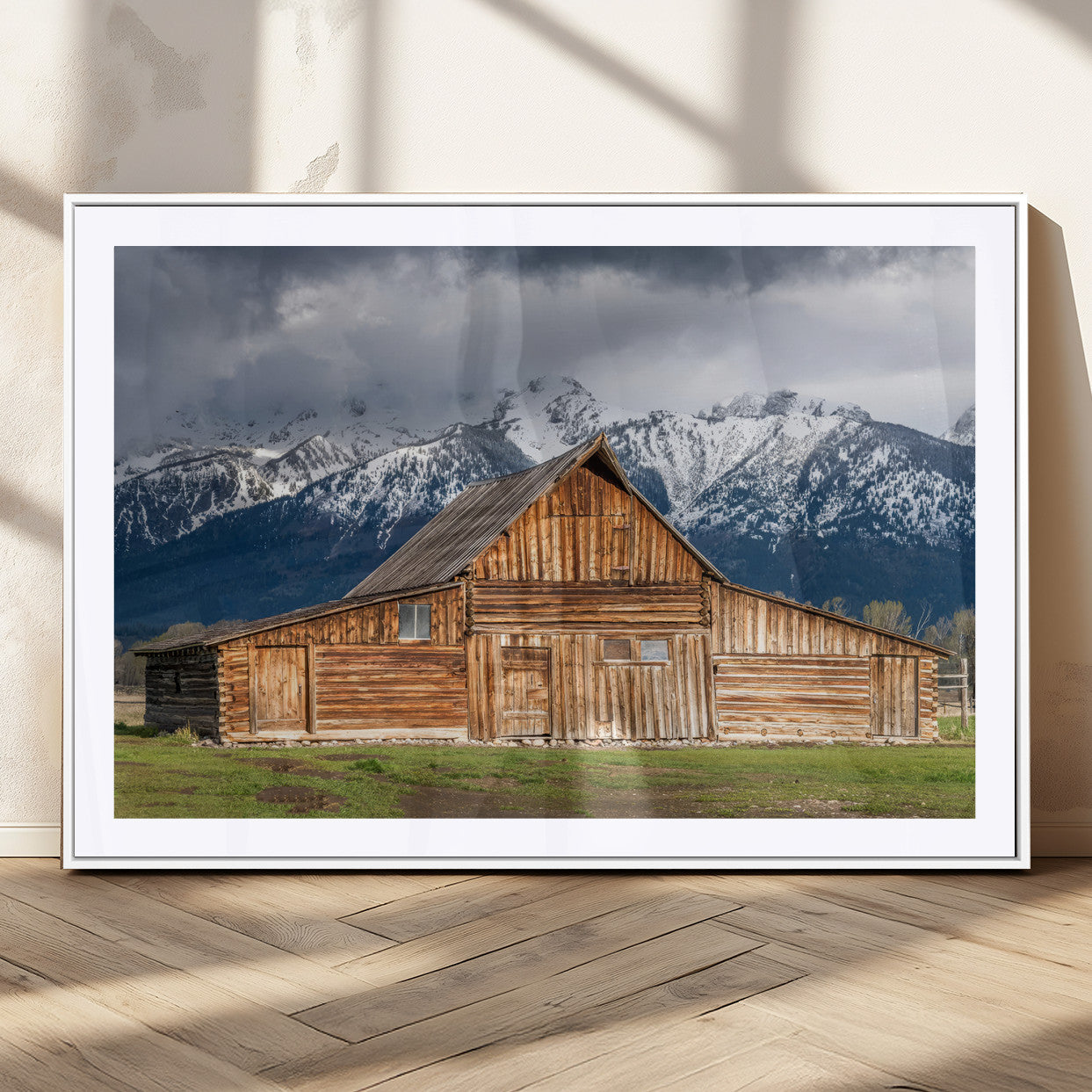 A stunning wall art canvas print featuring a rustic wooden barn set against a backdrop of snow-capped mountains under a dramatic cloudy sky, perfect for adding a touch of rural charm to any space.