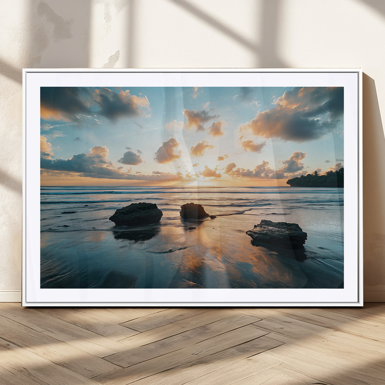A serene beach at sunset with vibrant clouds, calm water, and rocks in the foreground reflecting the warm colors of the setting sun.