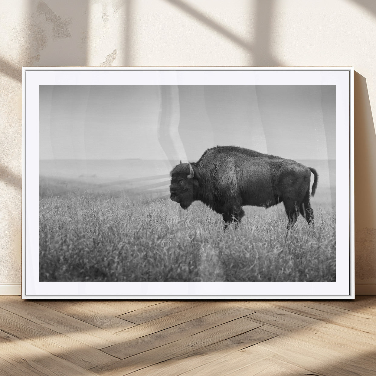 "Black and white image of a bison grazing in a vast field under an overcast sky."
