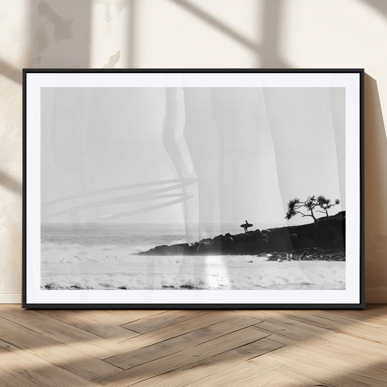 Black and white photo of a surfer standing on rocky cliffs, gazing at the waves, embodying the spirit of adventure and solitude.