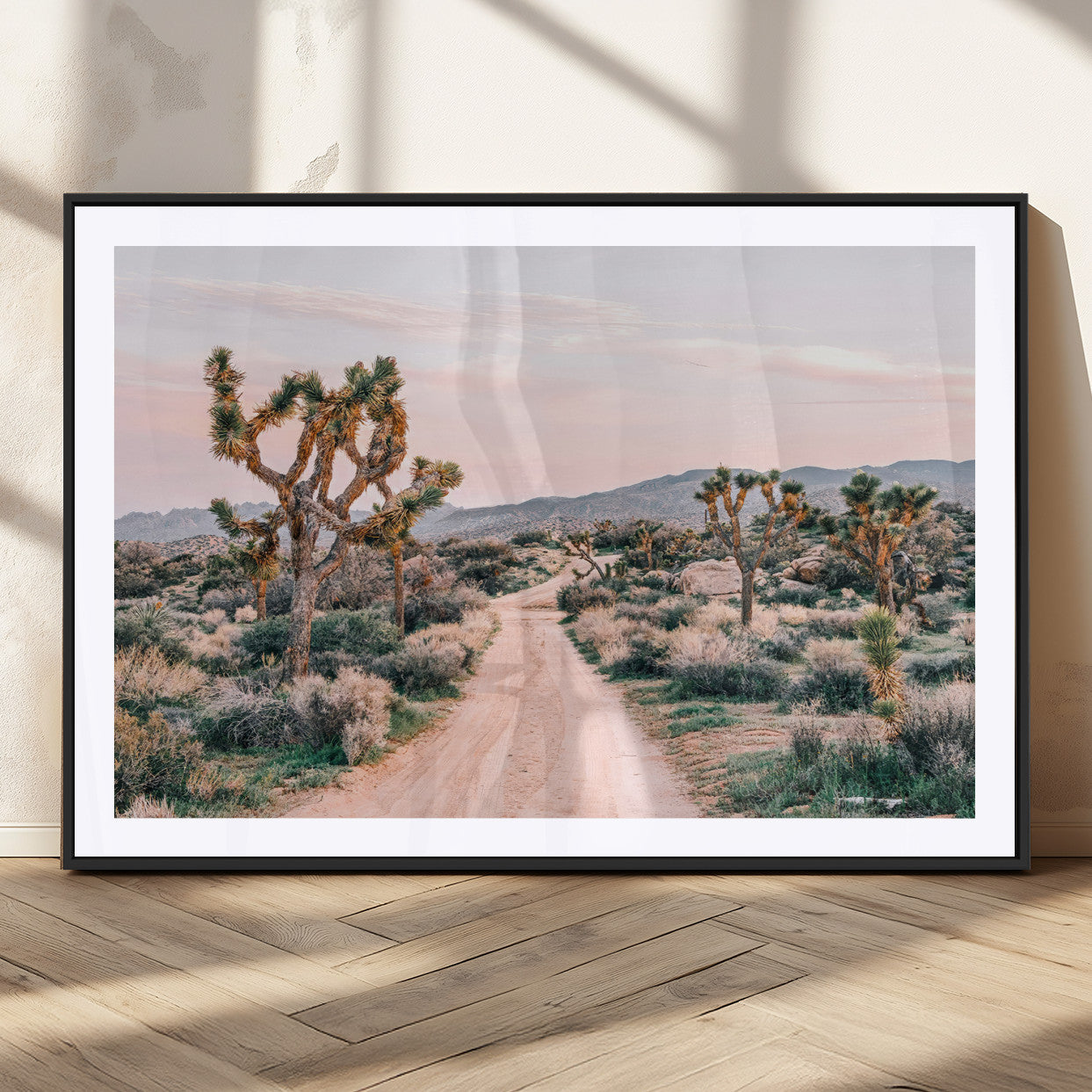 A dusty road winding through Joshua Tree National Park, framed by iconic twisted trees and warm desert tones under a soft pastel sky.