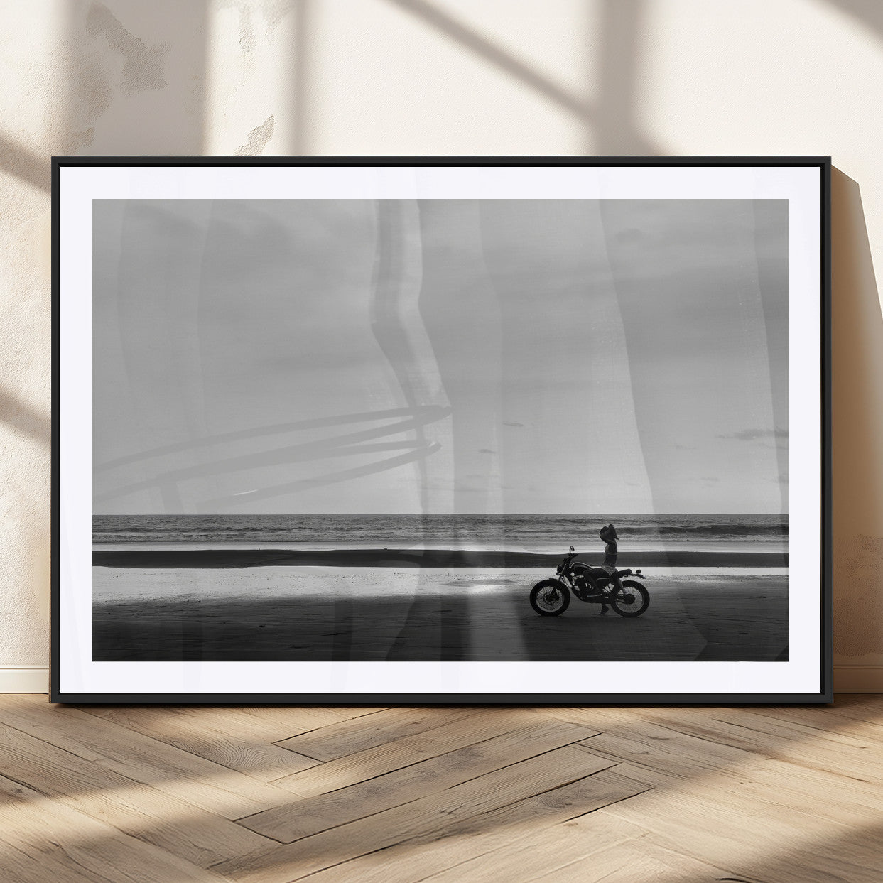 A motorcyclist on a vast beach, gazing at the ocean, capturing a moody and tranquil coastal adventure in black and white.