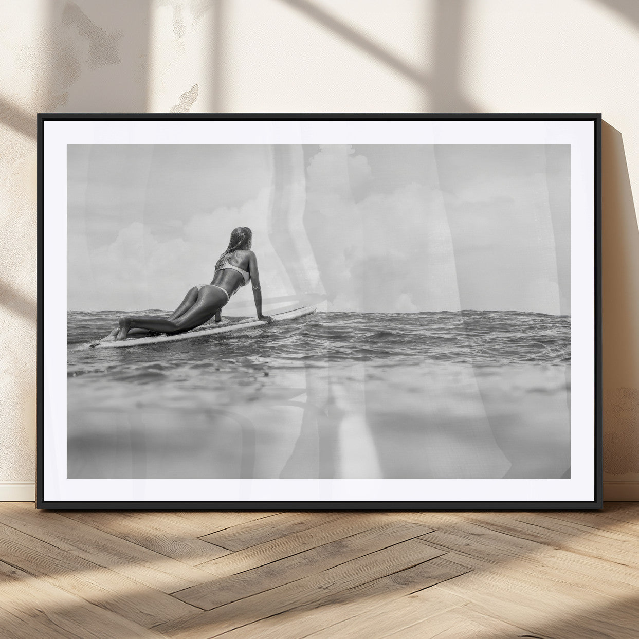 A black and white ocean scene featuring a surfer girl waiting on her board, gazing at the horizon, capturing a tranquil and adventurous coastal moment.