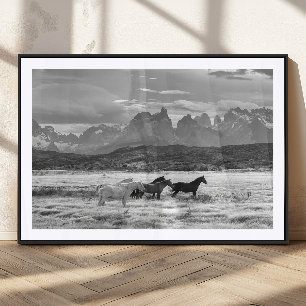 A black and white landscape of wild horses grazing in a vast grassland with towering mountains in the background, creating a moody and rustic western aesthetic.