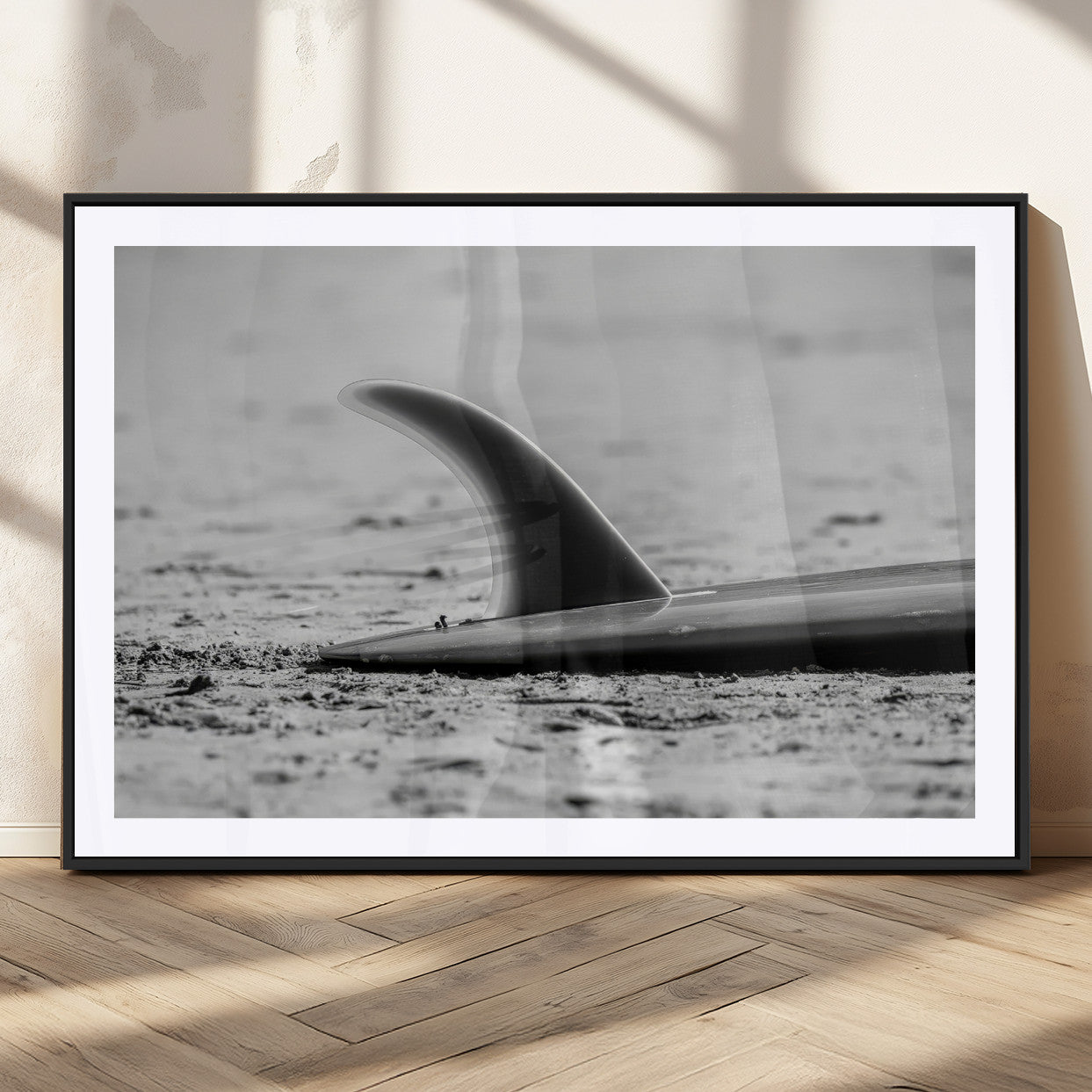 A black and white close-up of a surfboard fin resting on the sandy shore, highlighting minimalist beach aesthetics and classic surf culture.