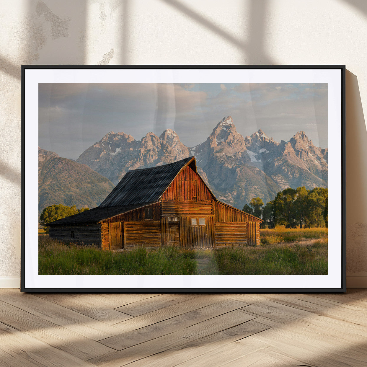 Rustic wooden barn set against towering mountain peaks under warm golden light, creating a peaceful Western countryside scene.