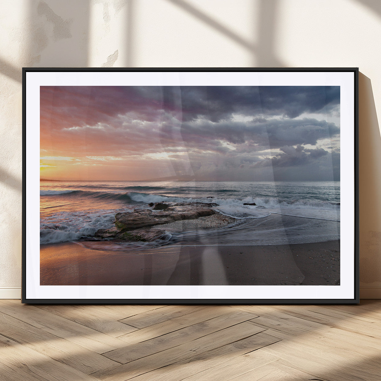 Dramatic sunset over a rocky shoreline with ocean waves gently reaching the sandy beach, creating a serene and coastal atmosphere.
