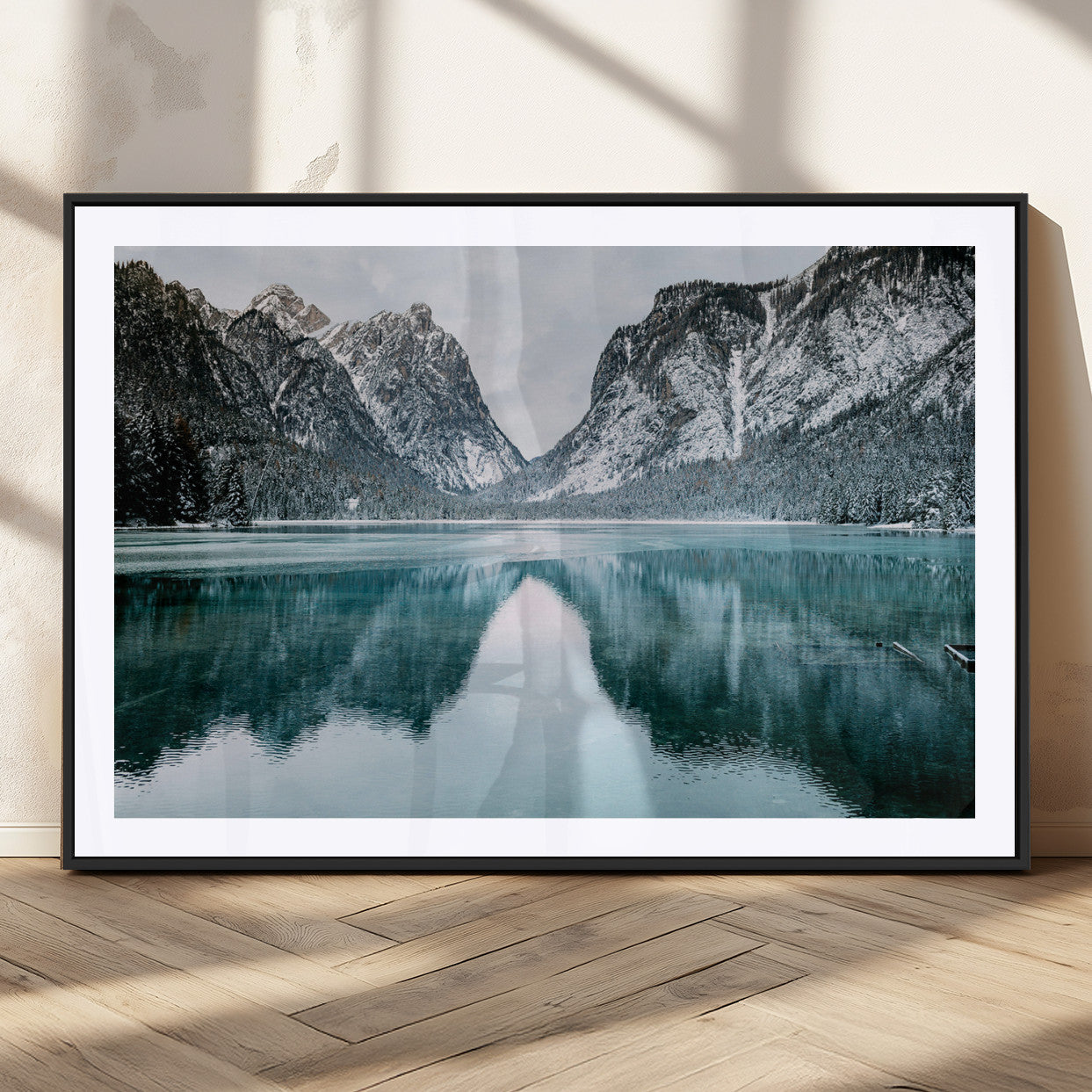Crystal-clear alpine lake reflecting snow-covered mountains, surrounded by evergreen trees, creating a serene and tranquil winter landscape.