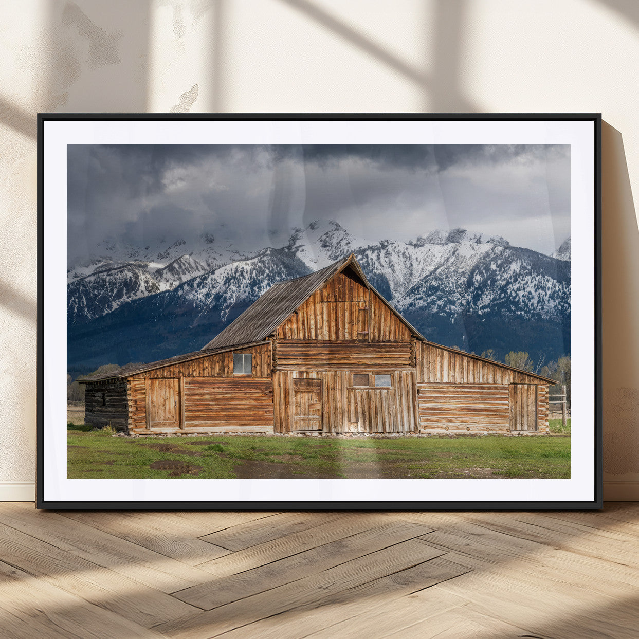 A stunning wall art canvas print featuring a rustic wooden barn set against a backdrop of snow-capped mountains under a dramatic cloudy sky, perfect for adding a touch of rural charm to any space.