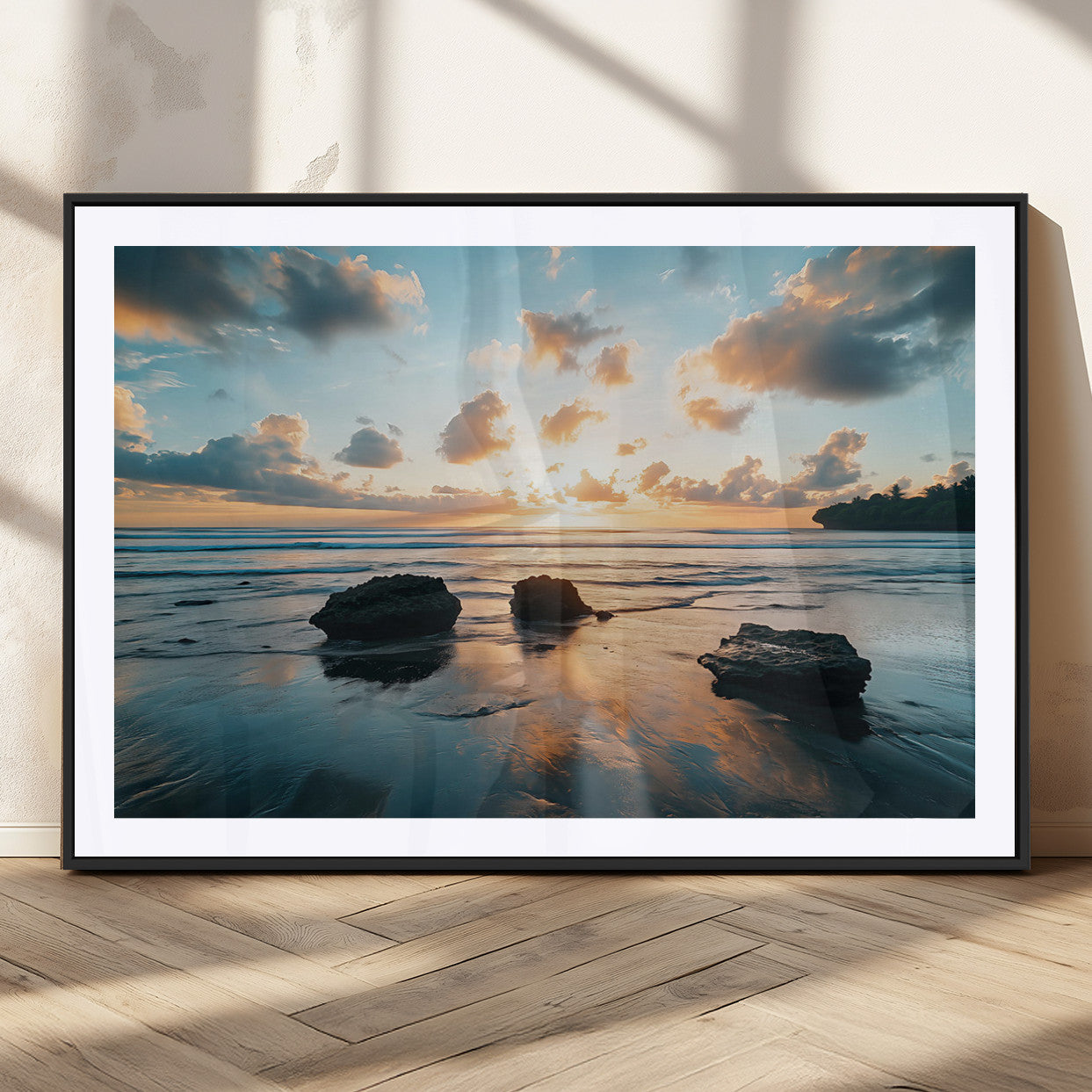 A serene beach at sunset with vibrant clouds, calm water, and rocks in the foreground reflecting the warm colors of the setting sun.