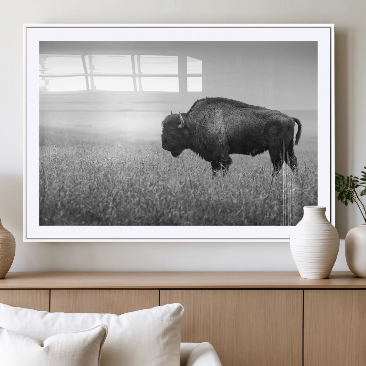 "Black and white image of a bison grazing in a vast field under an overcast sky."