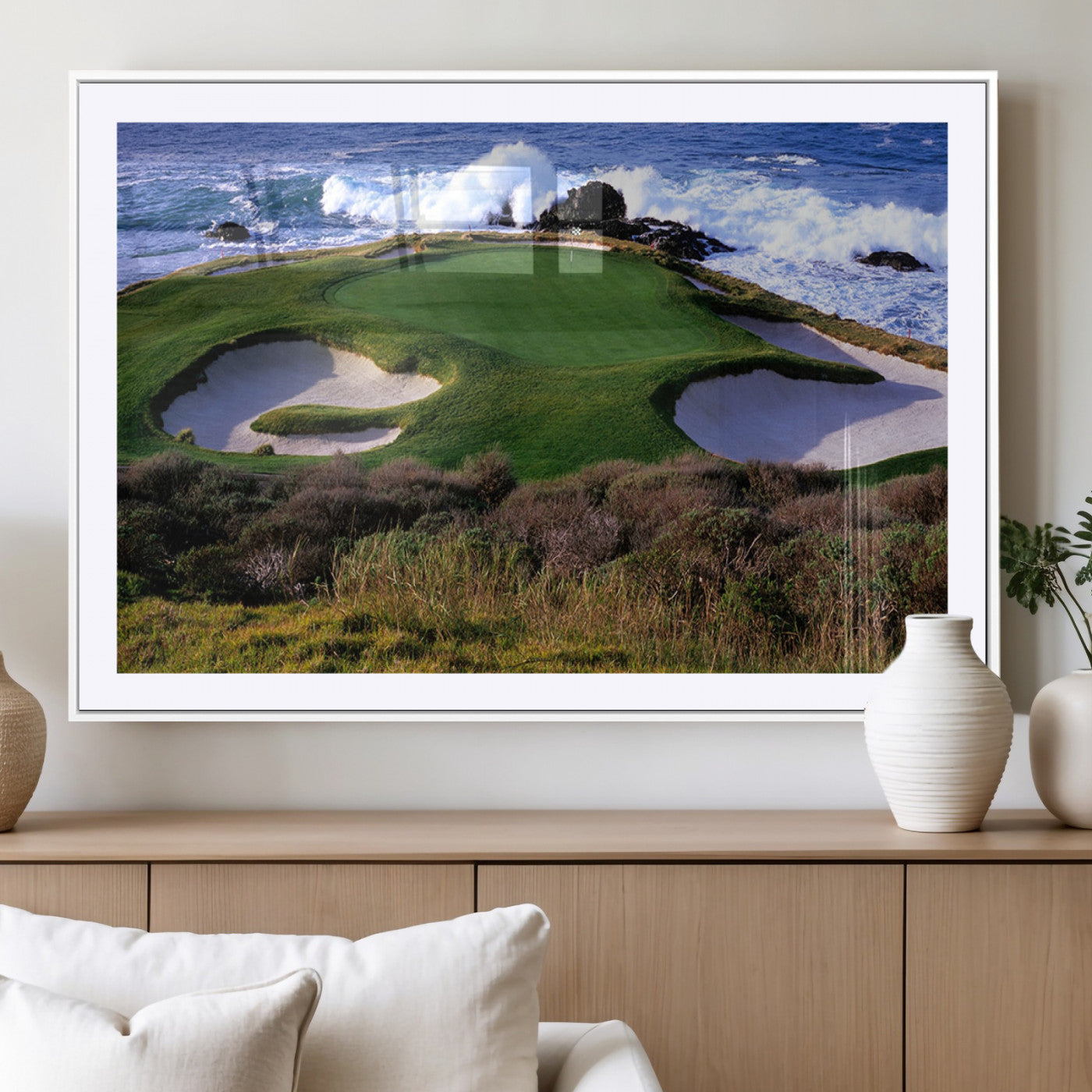 A scenic golf course located by the ocean, featuring a well-manicured green surrounded by sand traps and powerful ocean waves crashing on the shore.