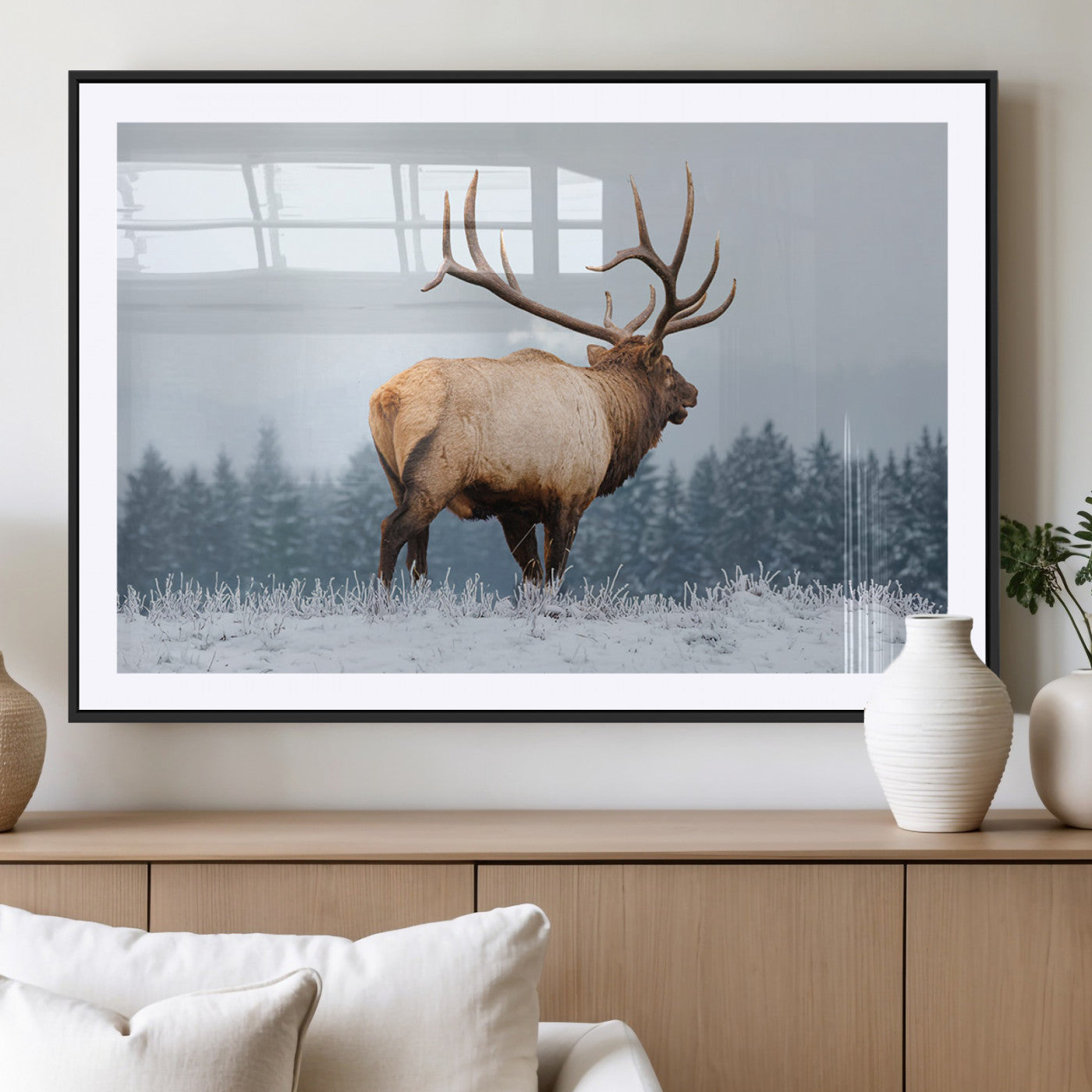 A majestic elk standing in a snowy landscape, with large antlers, set against a backdrop of evergreen trees and a soft winter sky.