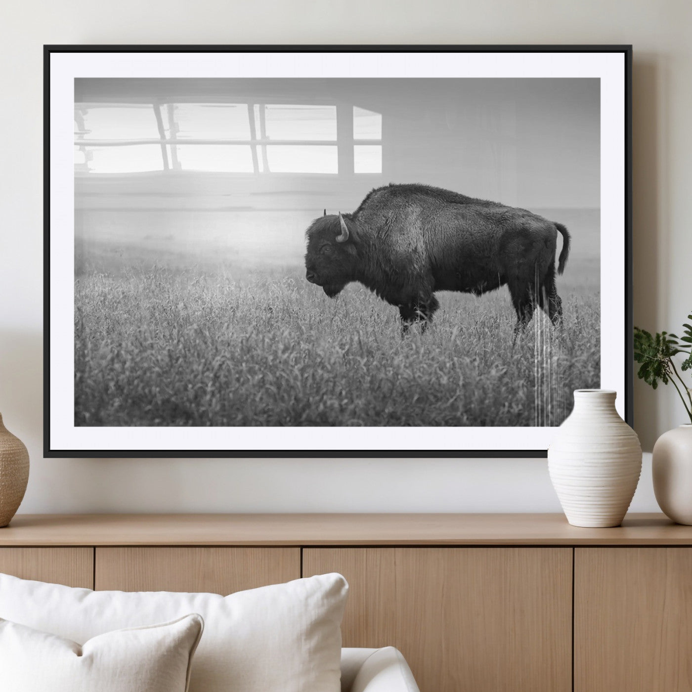 "Black and white image of a bison grazing in a vast field under an overcast sky."