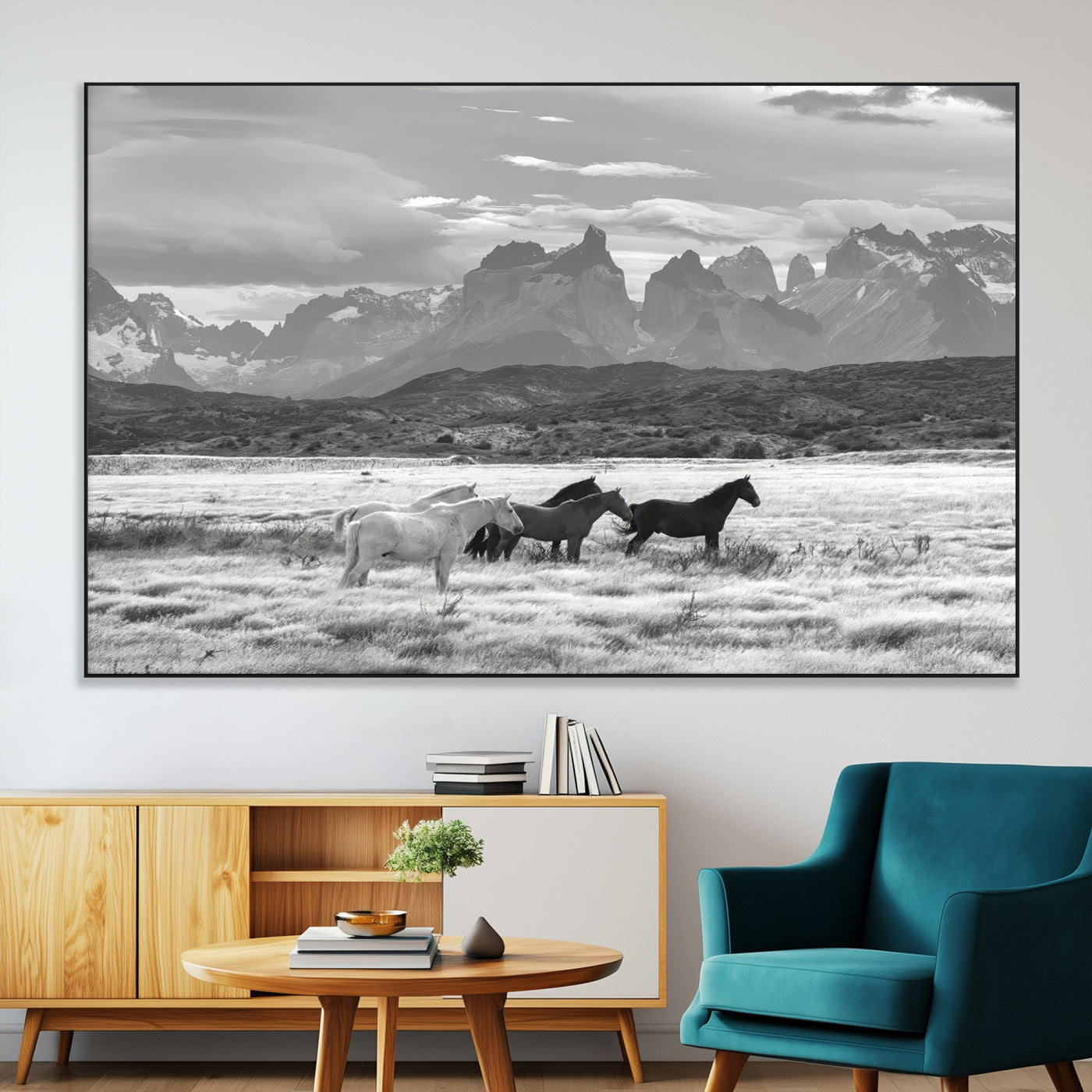 A black and white landscape of wild horses grazing in a vast grassland with towering mountains in the background, creating a moody and rustic western aesthetic.