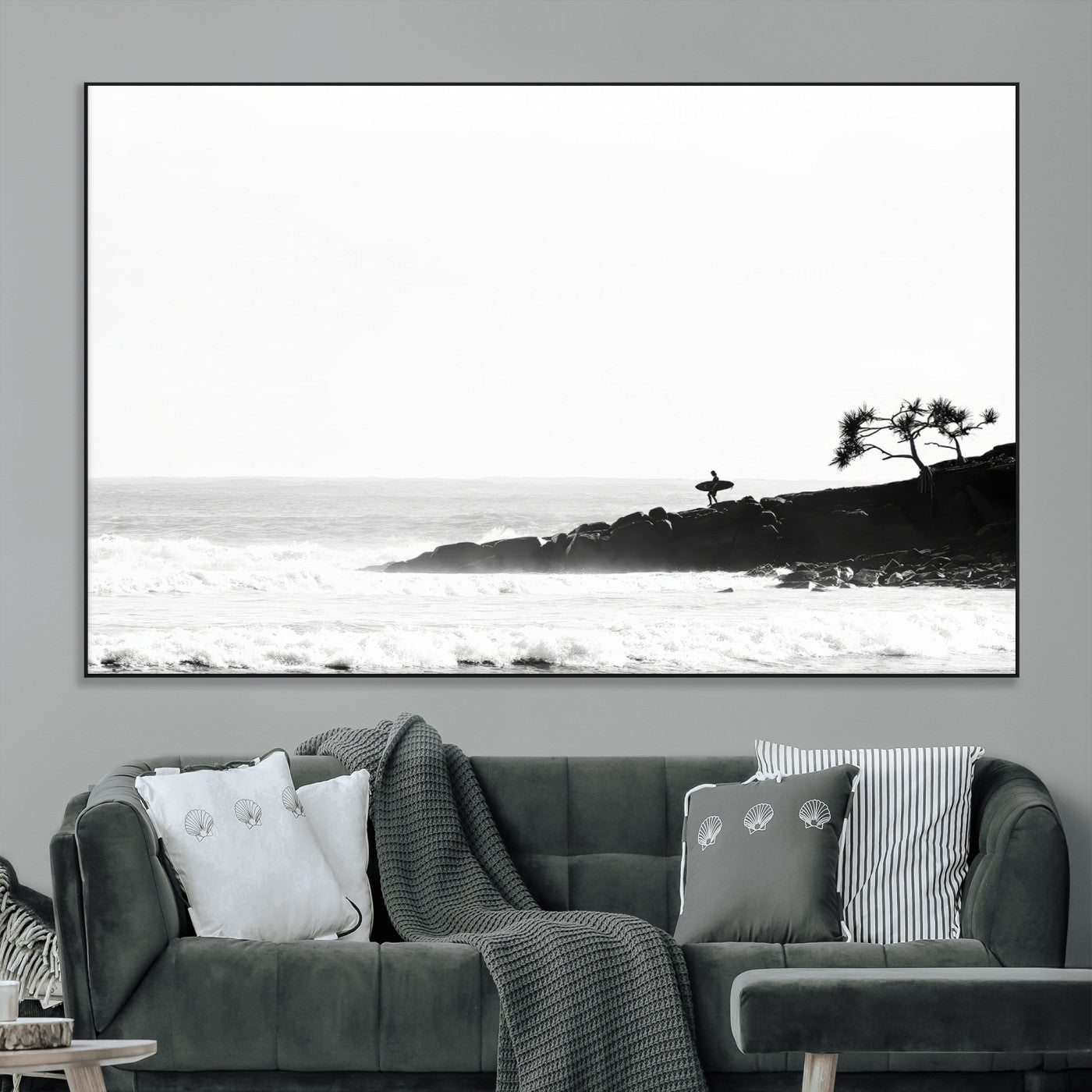 Black and white photo of a surfer standing on rocky cliffs, gazing at the waves, embodying the spirit of adventure and solitude.