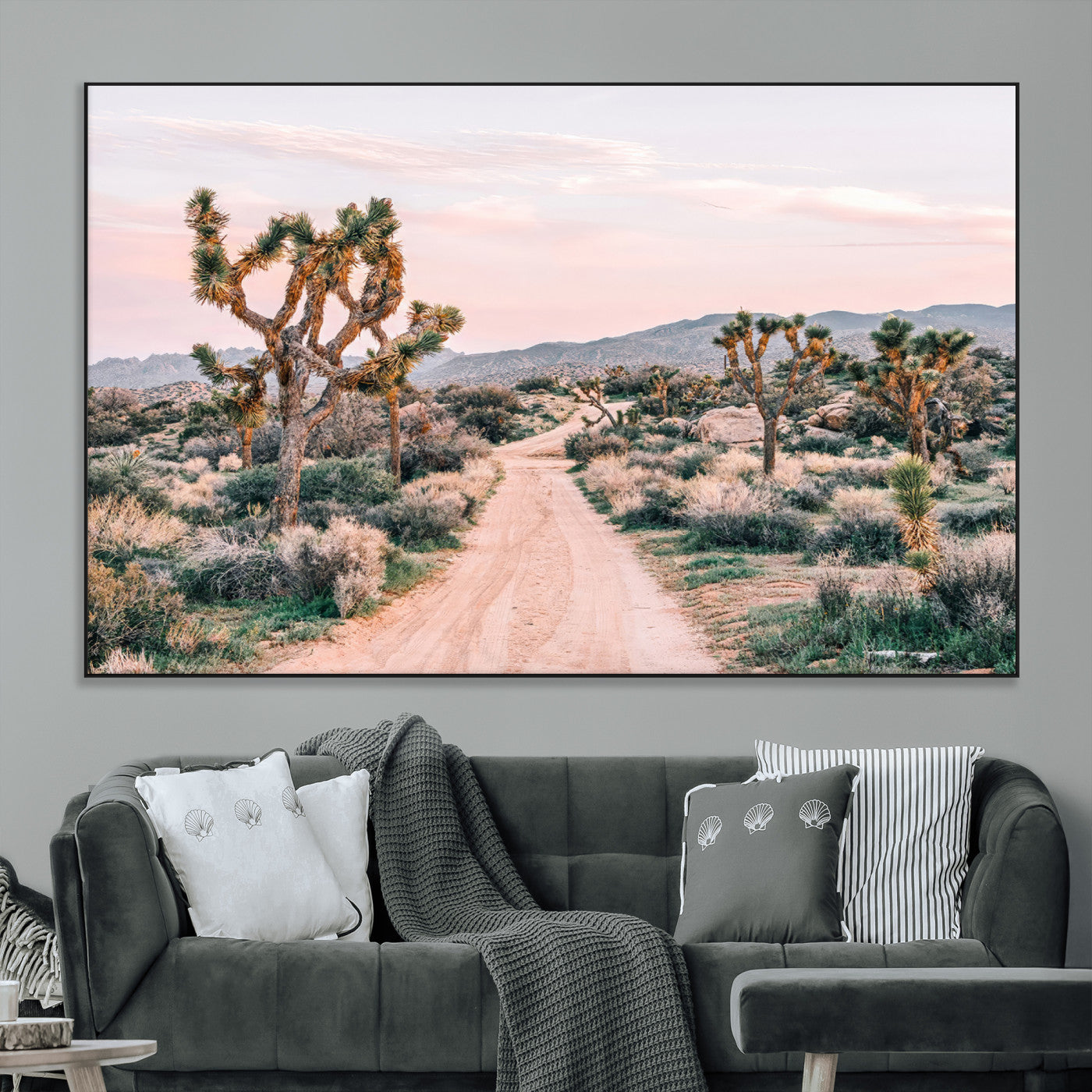 A dusty road winding through Joshua Tree National Park, framed by iconic twisted trees and warm desert tones under a soft pastel sky.