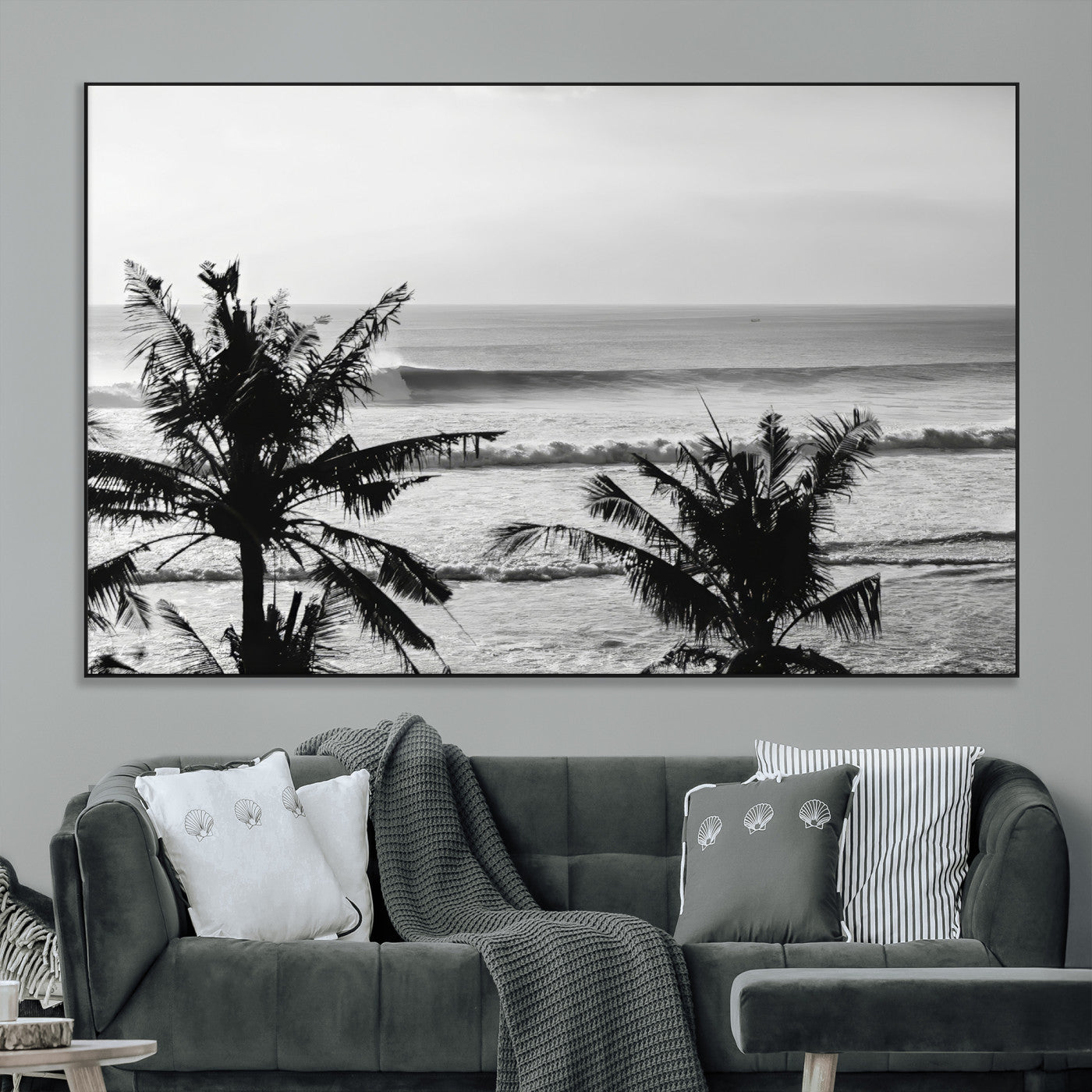 Black and white view of ocean waves crashing on a tropical coastline, framed by silhouetted palm trees under a vast, open sky.