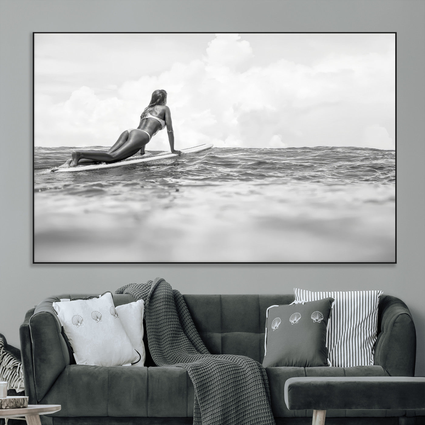 A black and white ocean scene featuring a surfer girl waiting on her board, gazing at the horizon, capturing a tranquil and adventurous coastal moment.