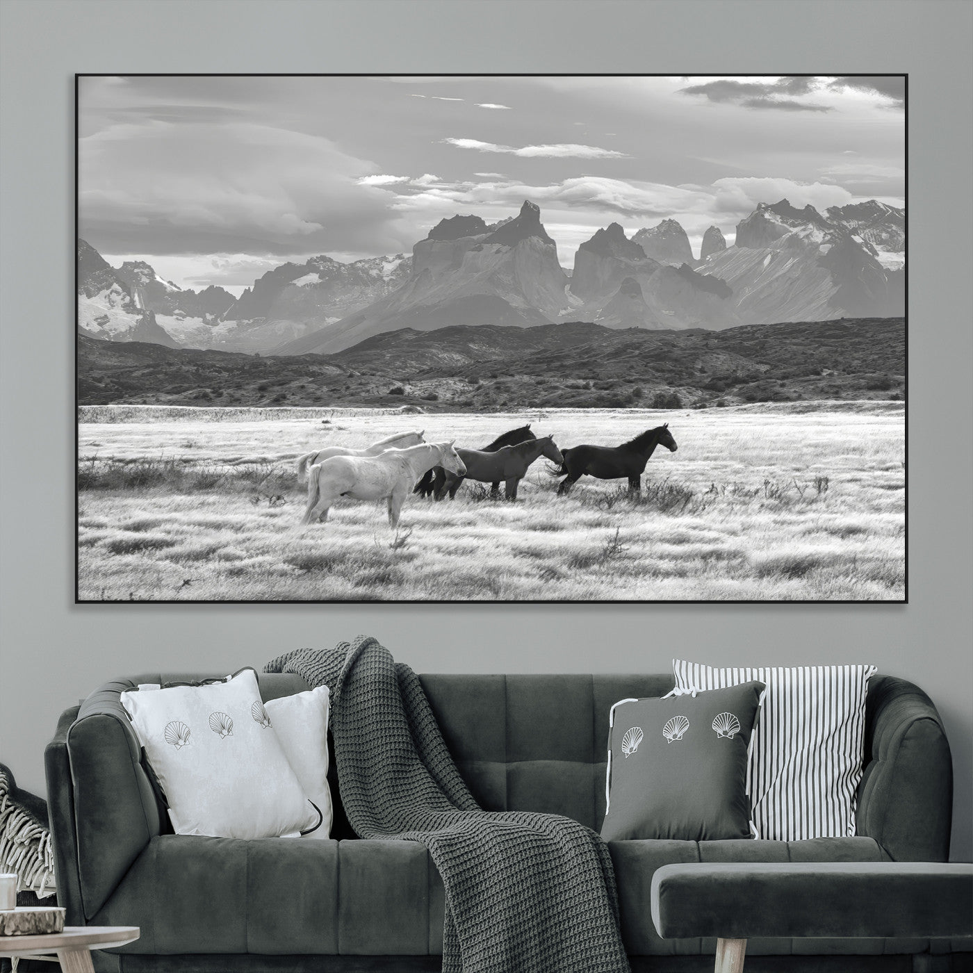 A black and white landscape of wild horses grazing in a vast grassland with towering mountains in the background, creating a moody and rustic western aesthetic.
