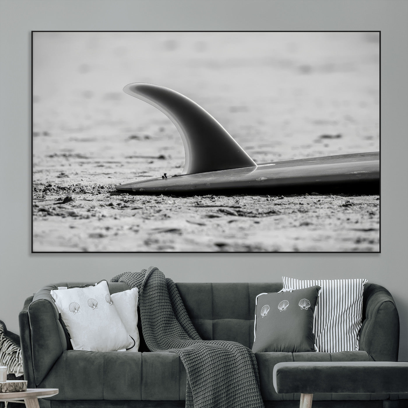 A black and white close-up of a surfboard fin resting on the sandy shore, highlighting minimalist beach aesthetics and classic surf culture.