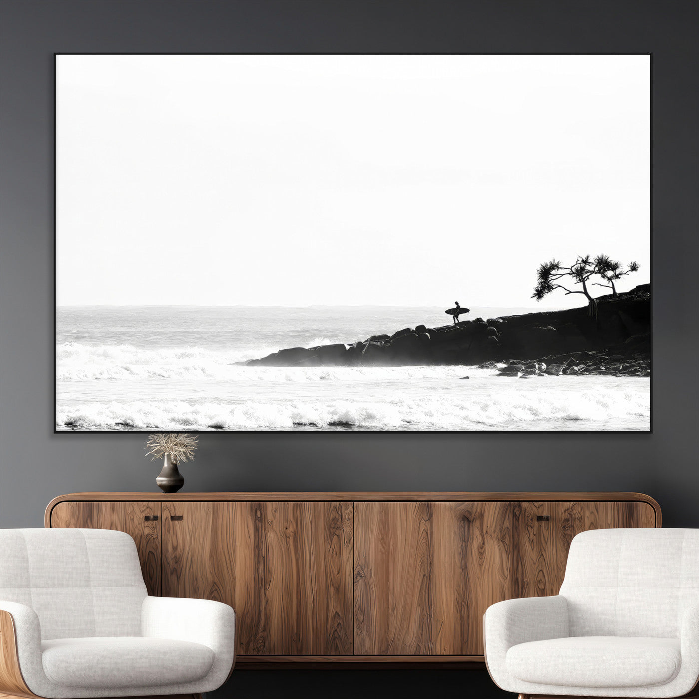 Black and white photo of a surfer standing on rocky cliffs, gazing at the waves, embodying the spirit of adventure and solitude.