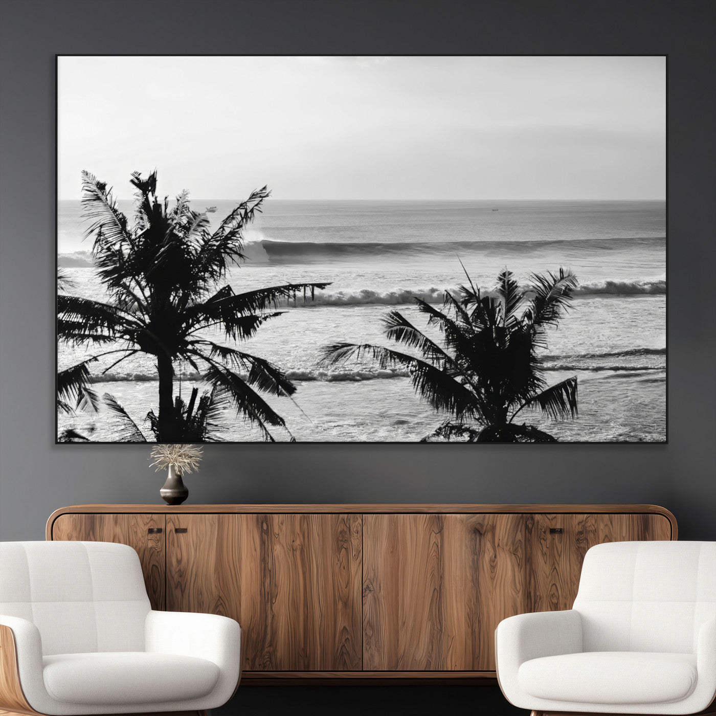 Black and white view of ocean waves crashing on a tropical coastline, framed by silhouetted palm trees under a vast, open sky.